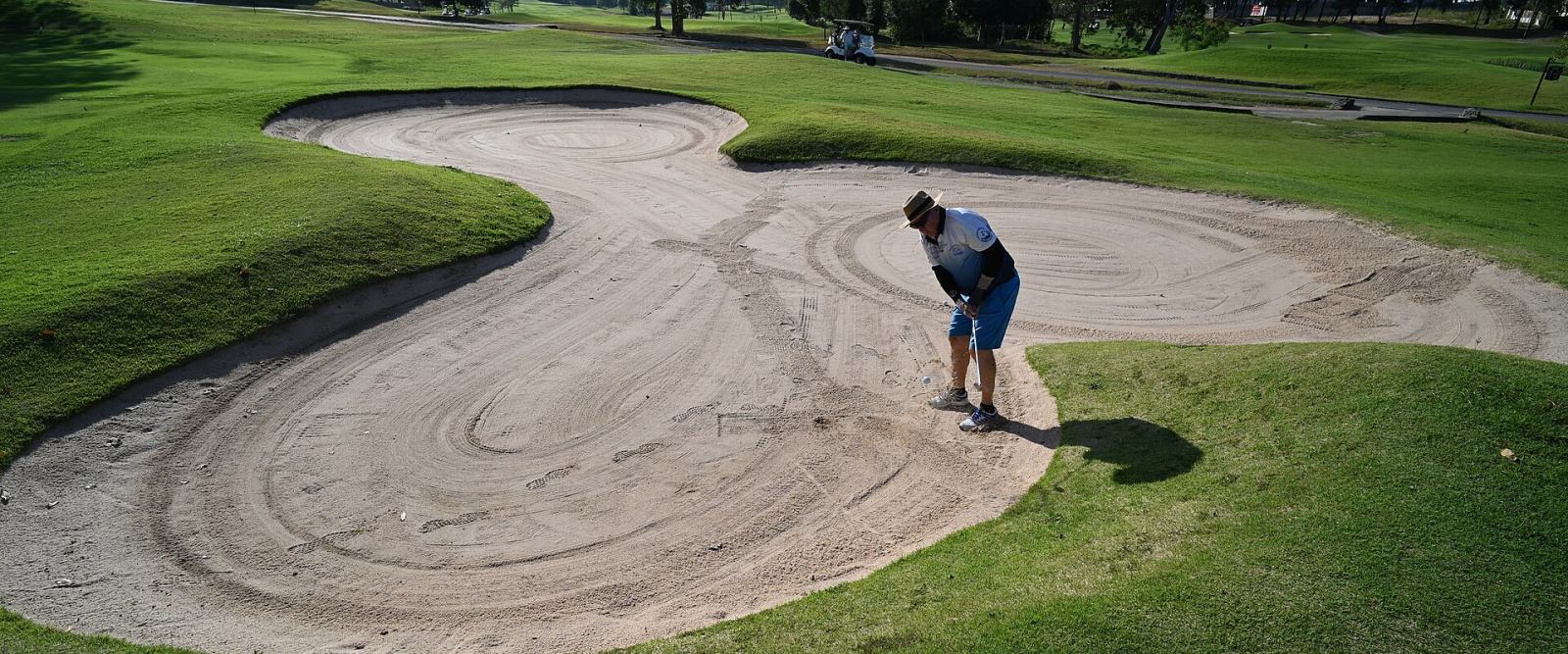 A golfer playing out of a bunker on a sunlit course
