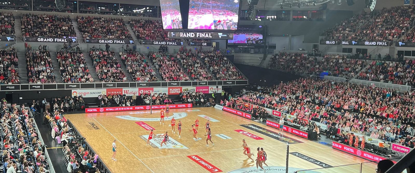 A netball grand final in play on a floodlit indoor court